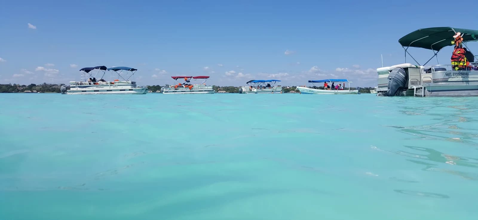 Pontoon tour boats with shade canopies anchored on the shallow turquoise water of the Pirate Channel, Bacalar