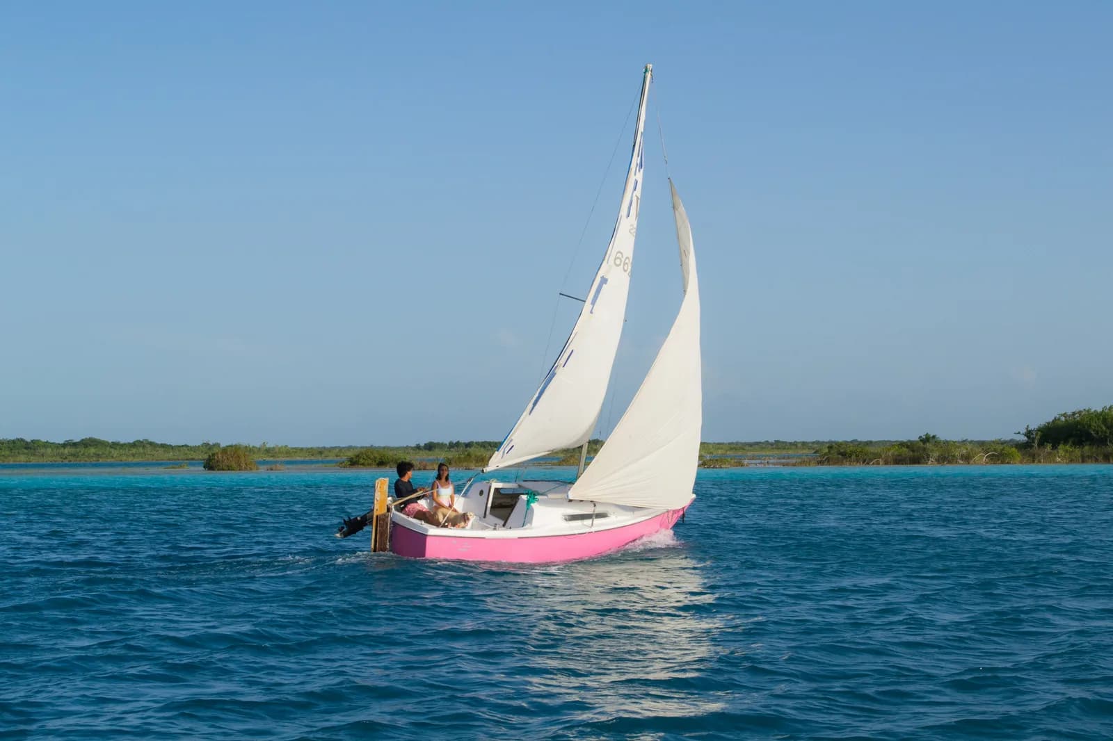 A small sailboat crossing the turquoise water of the Bacalar lagoon in Quintana Roo, Mexico
