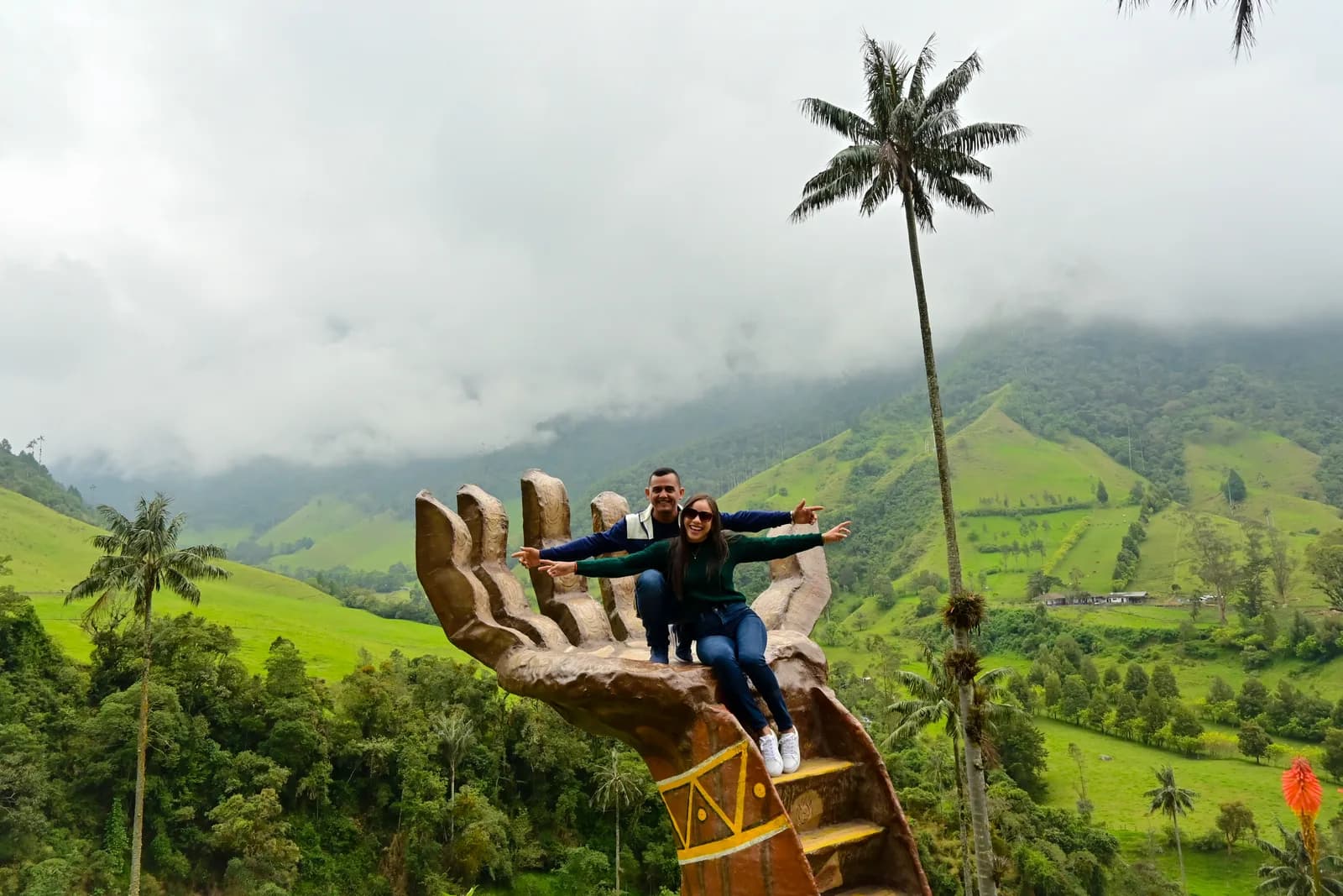 Visitors sitting in the giant hand sculpture at the Mirador Mano de Acaime viewpoint above the Cocora Valley, Colombia