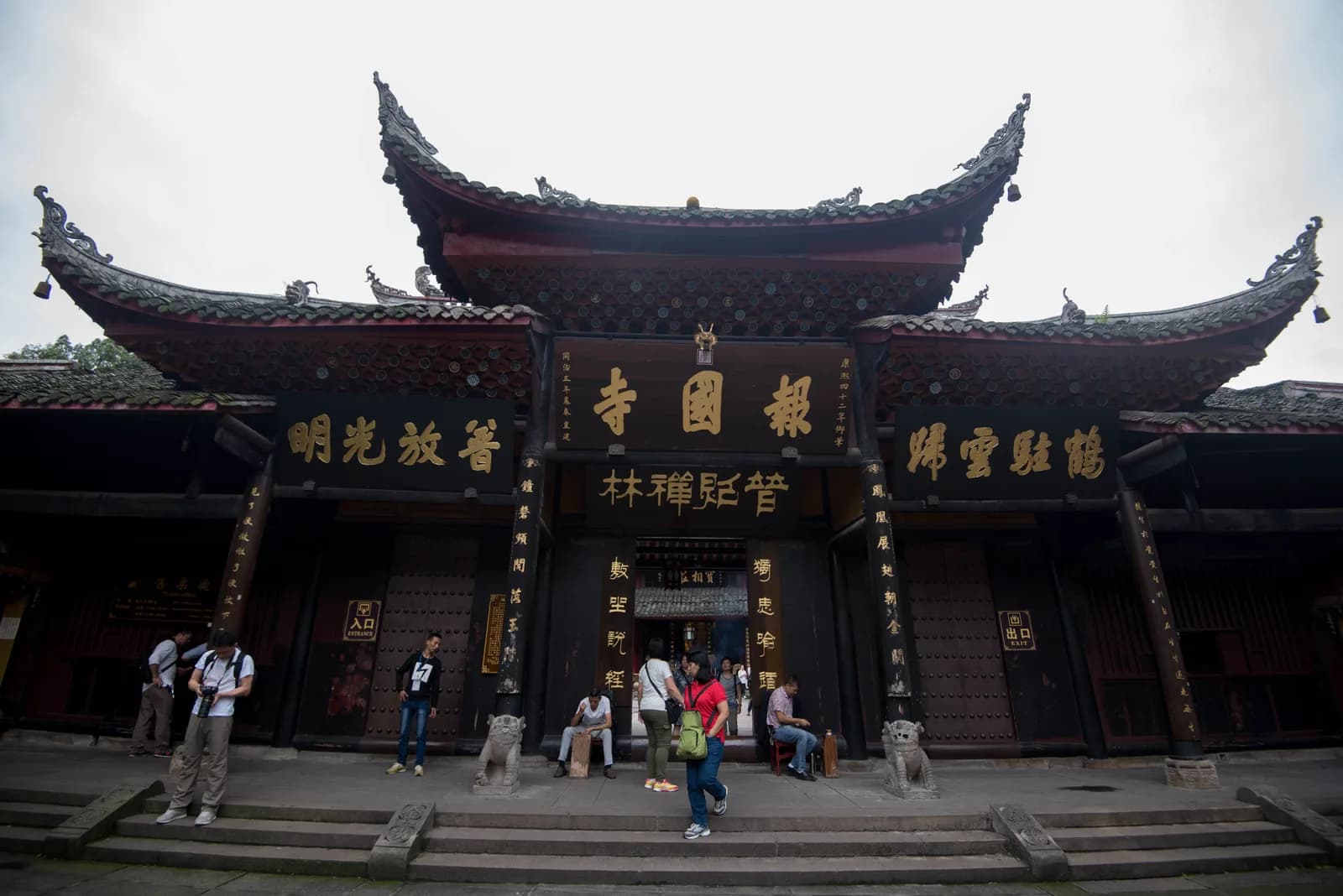 The entrance gate of Baoguo Temple at the foot of Mount Emei, with stone steps and forested hillside behind