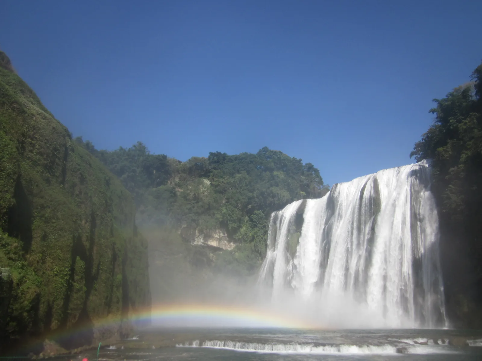 Huangguoshu Waterfall thundering over its limestone cliff into the green pool below, framed by karst hills