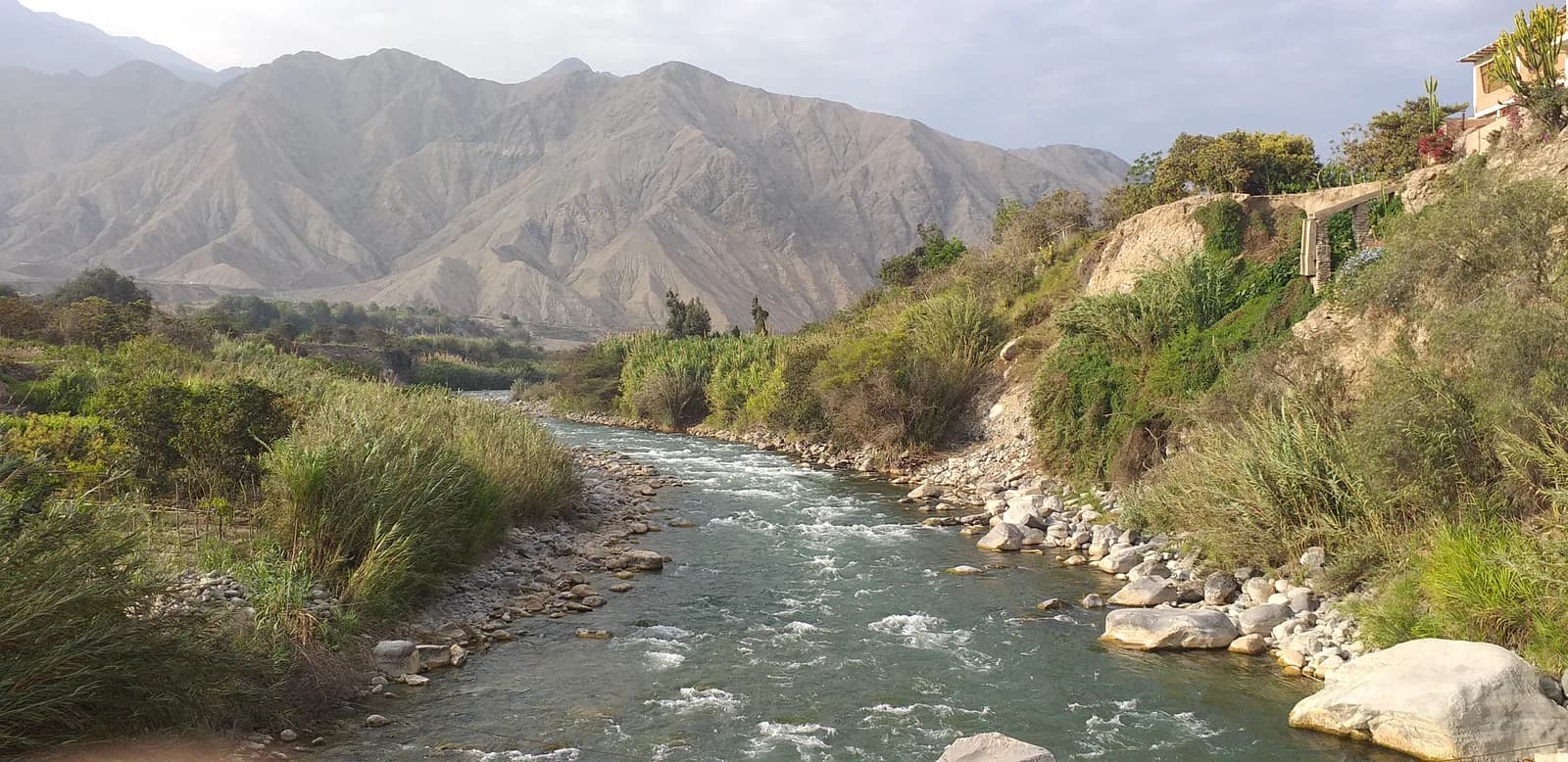 The Río Cañete running fast over rocks below the Catapalla hanging bridge in the Lunahuaná valley, dry Andean hills behind
