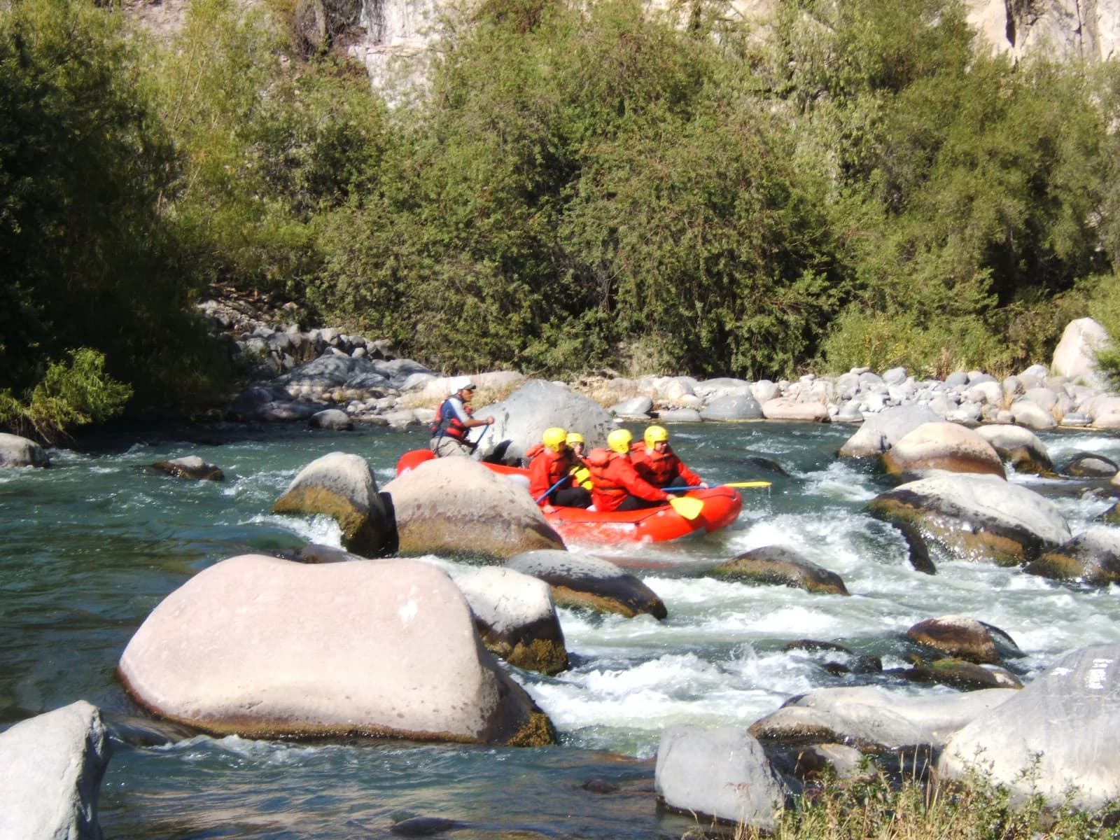 A raft of paddlers in red life jackets and yellow helmets running a boulder-strewn rapid on Peru's Río Chili near Arequipa