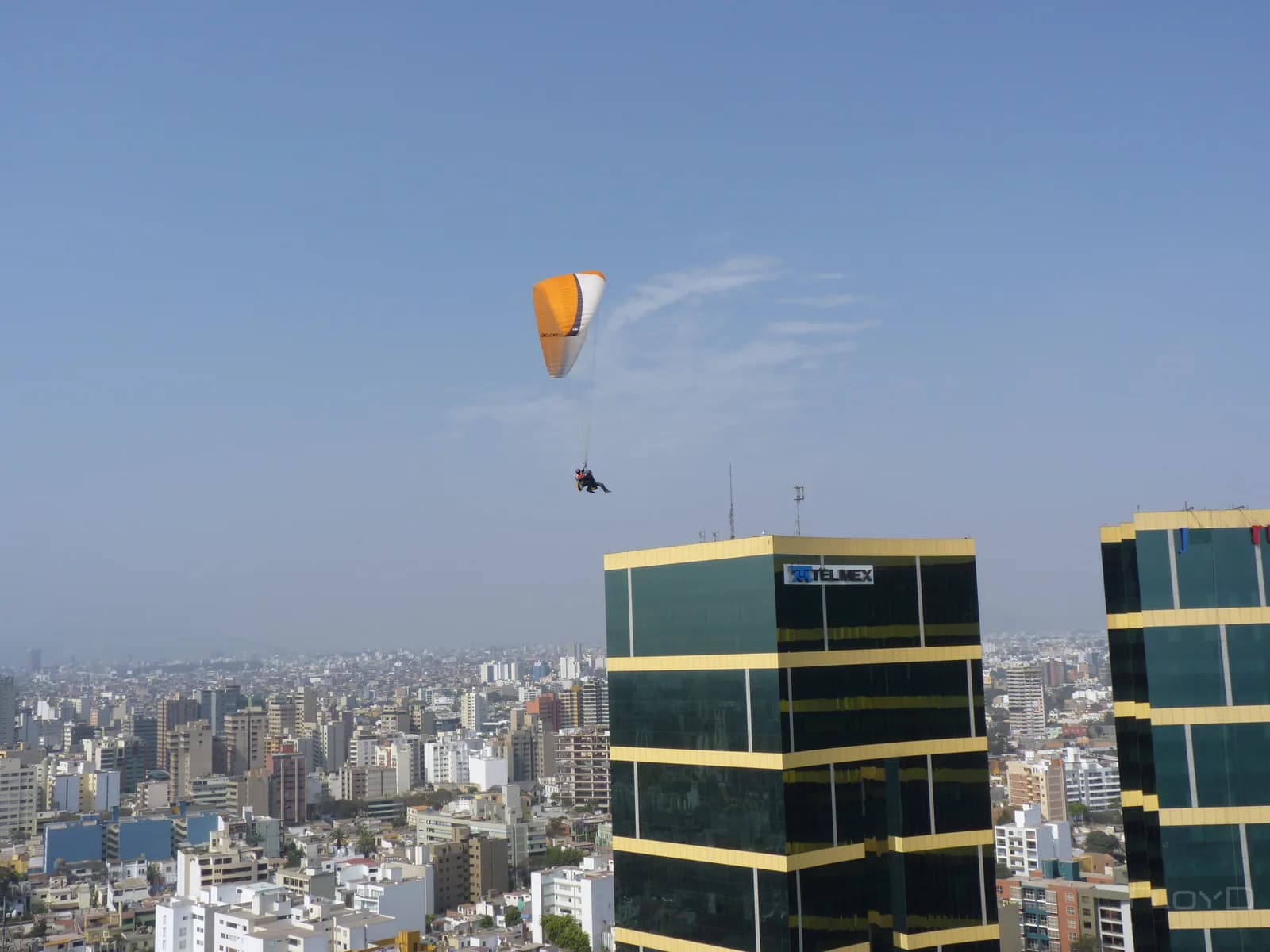 A tandem paraglider soaring over the Miraflores clifftop and high-rise skyline above the Pacific in Lima, Peru