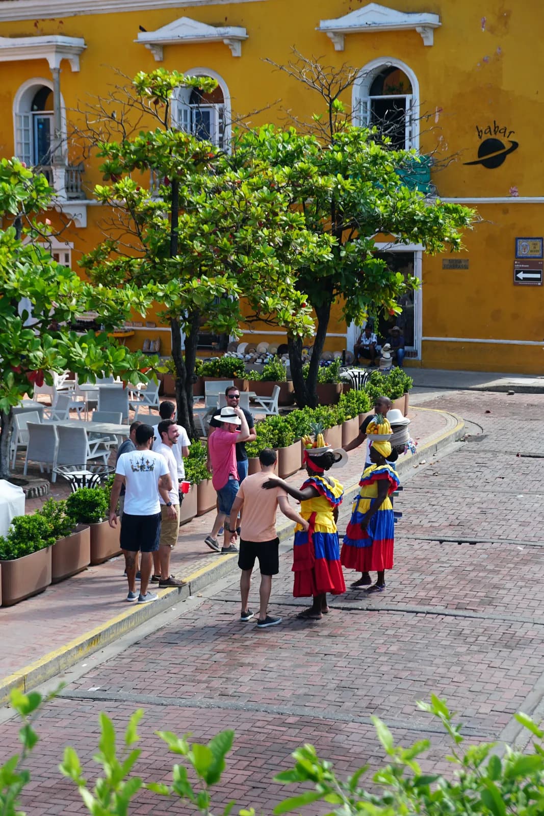 Palenquera women in colorful dresses with fruit bowls posing with tourists in Cartagena's old city