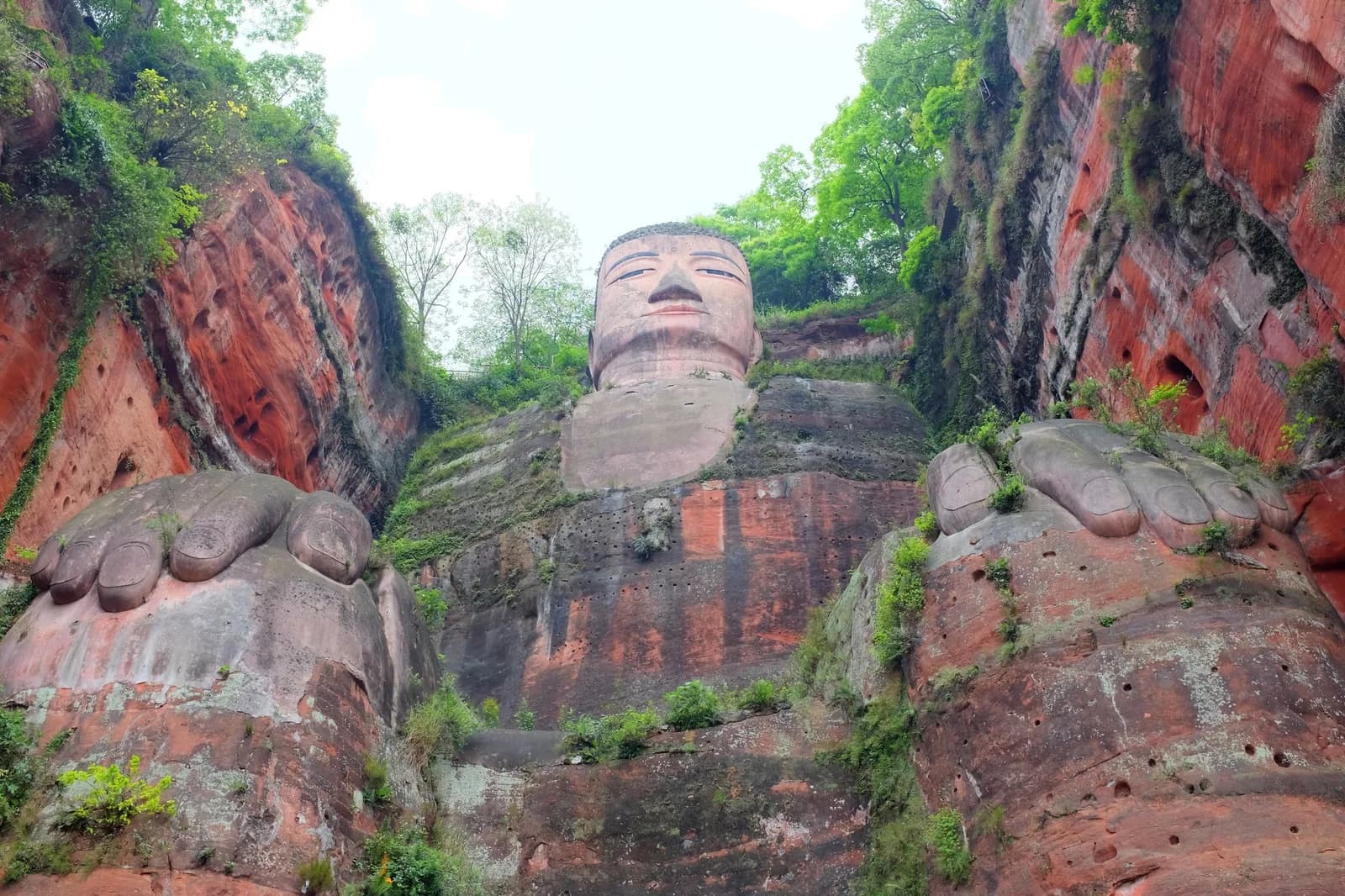 The Leshan Giant Buddha seen from below, its carved feet and full seated figure rising up the river cliff