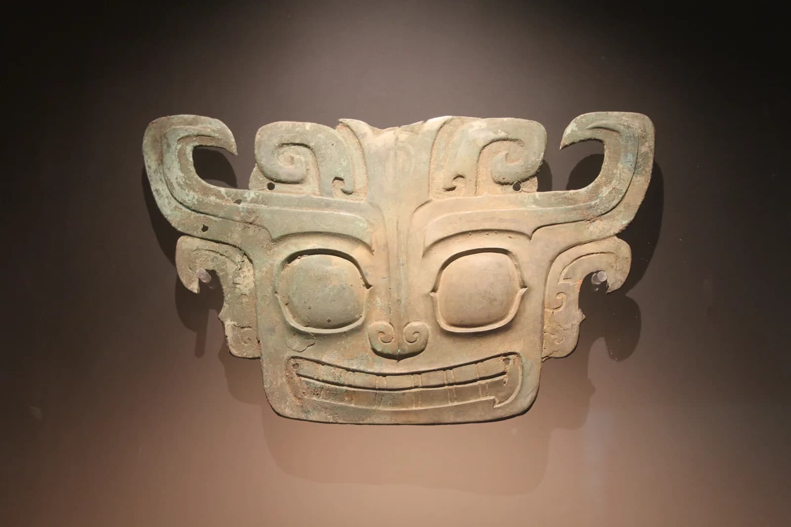 A 3,000-year-old bronze animal mask from the Sanxingdui archaeological site displayed against a dark background