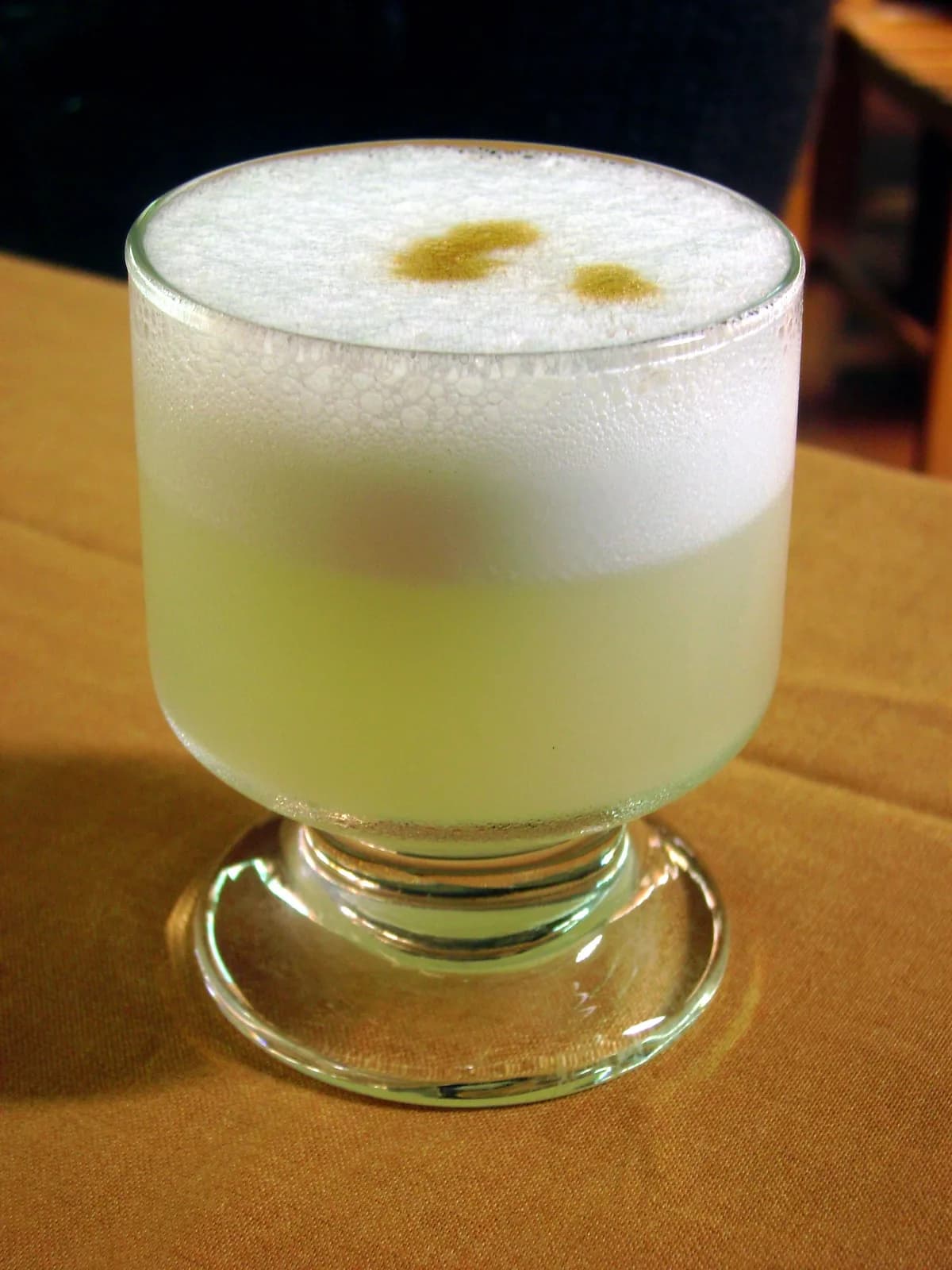 A frothy pisco sour in a tall glass, the classic Peruvian cocktail made with pisco, lime and egg white