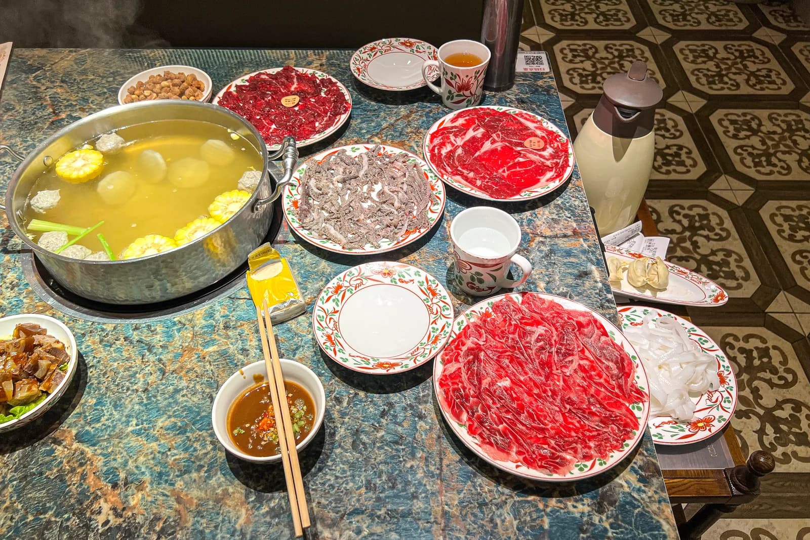 Plates of Chaoshan beef hotpot cuts arranged around a clear broth pot, each cut plated separately