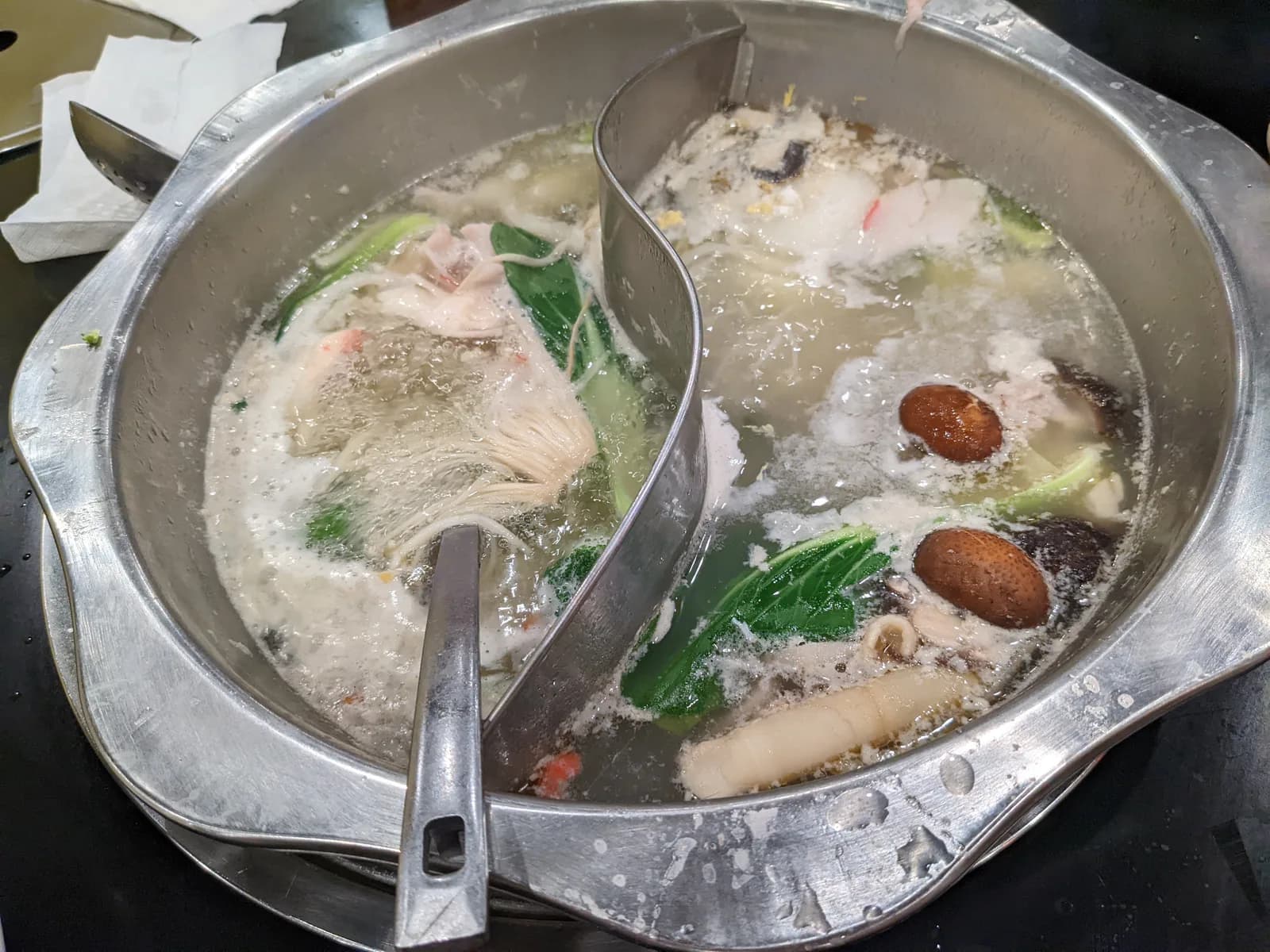 A bubbling divided Sichuan hotpot with spicy red broth on one side and clear broth on the other, surrounded by raw ingredients