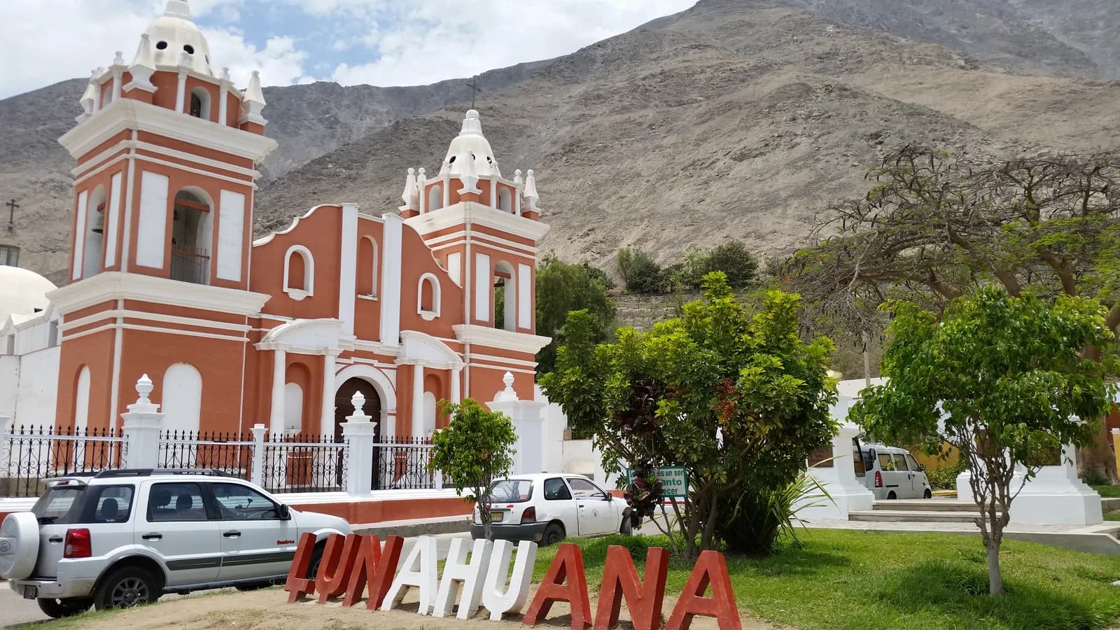 The red and white colonial church of Lunahuaná beside the plaza with the town's large letter sign and dry hills behind