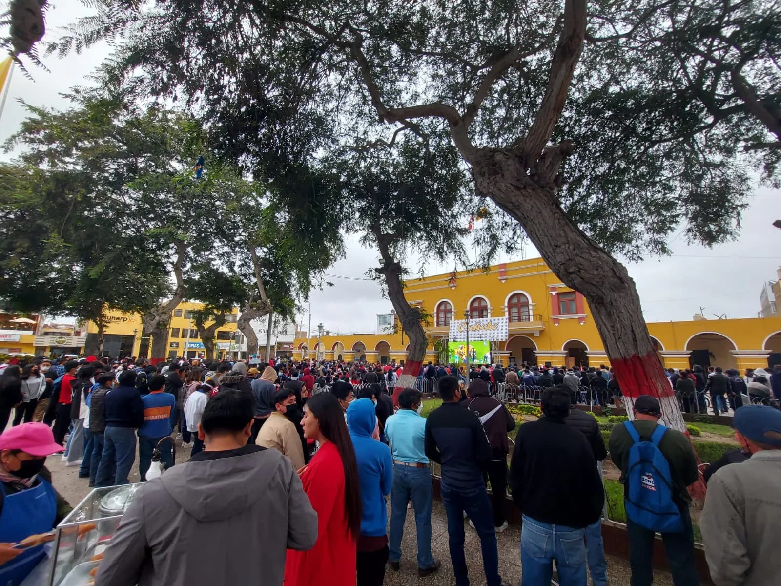 Crowds filling the main plaza of San Vicente de Cañete in front of yellow arcaded buildings and large trees