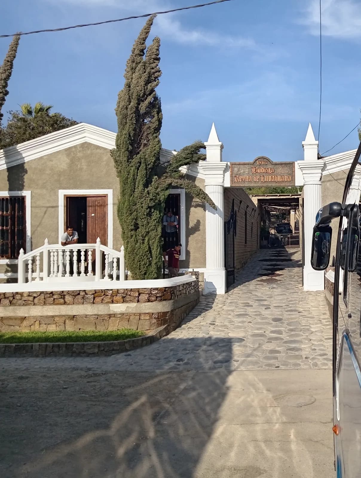 Entrance of Bodega Reina de Lunahuaná with white columns, stone paving and a sign over the walkway
