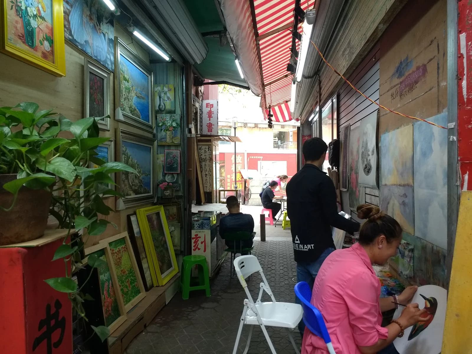 Painters working on canvases in a narrow lane of Dafen Oil Painting Village in Shenzhen