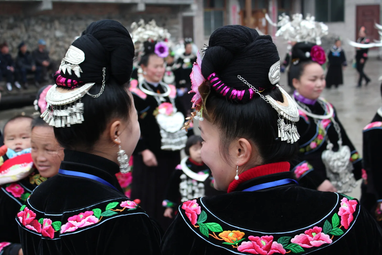 Miao women in embroidered festival dress and layered silver jewelry at a village festival in Leishan County