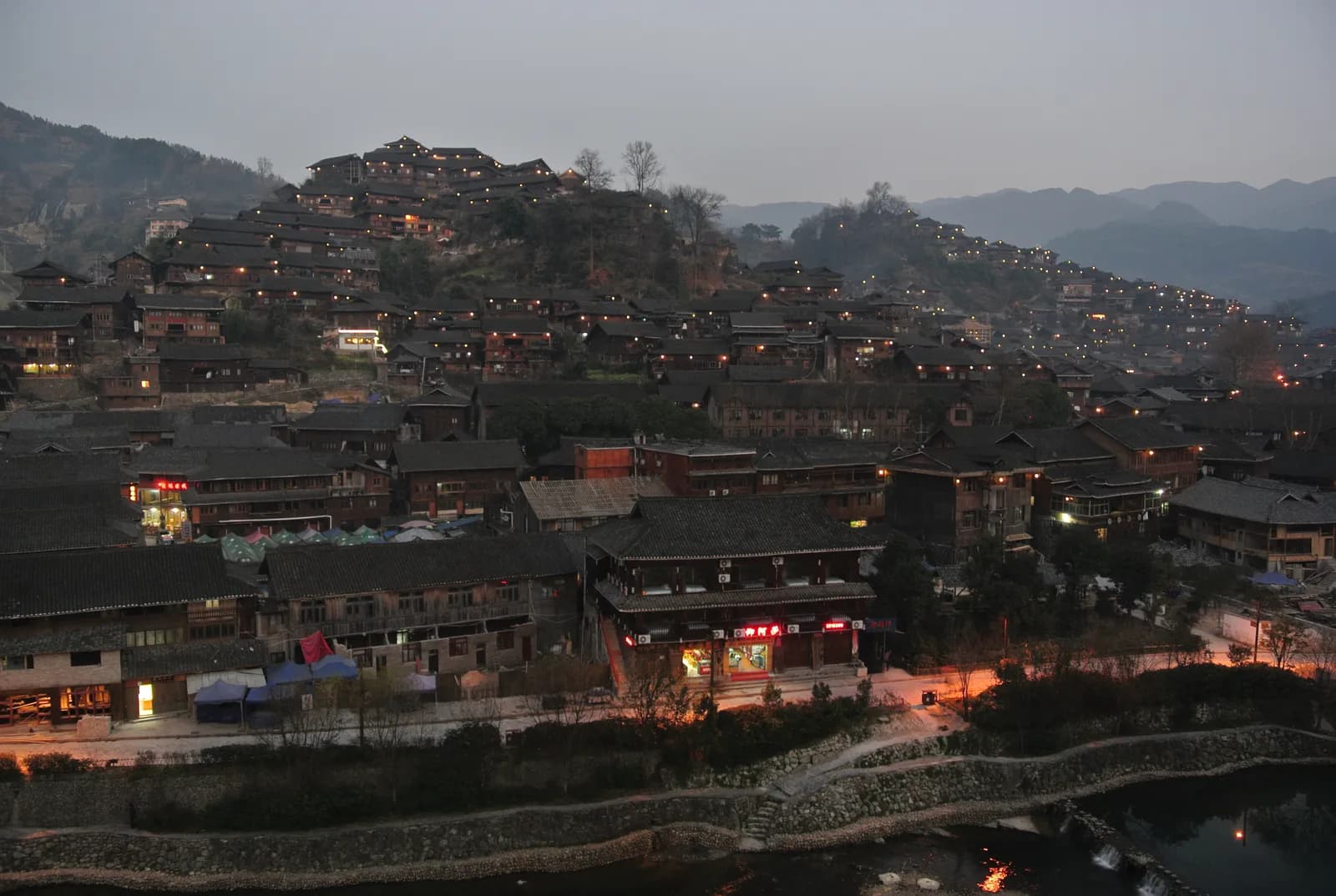 Evening falling over the tiled roofs and lit windows of Xijiang Miao Village in Guizhou